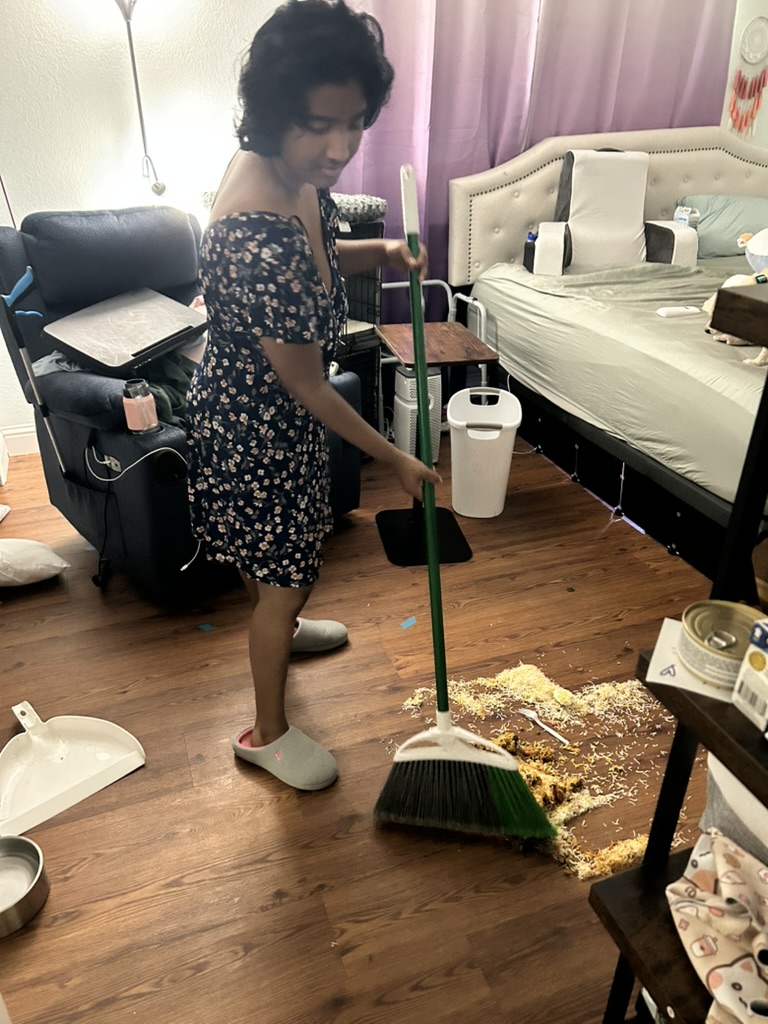 Harshini sweeping spilled food from the floor using a broom, with the surrounding area showing the aftermath of the accident.