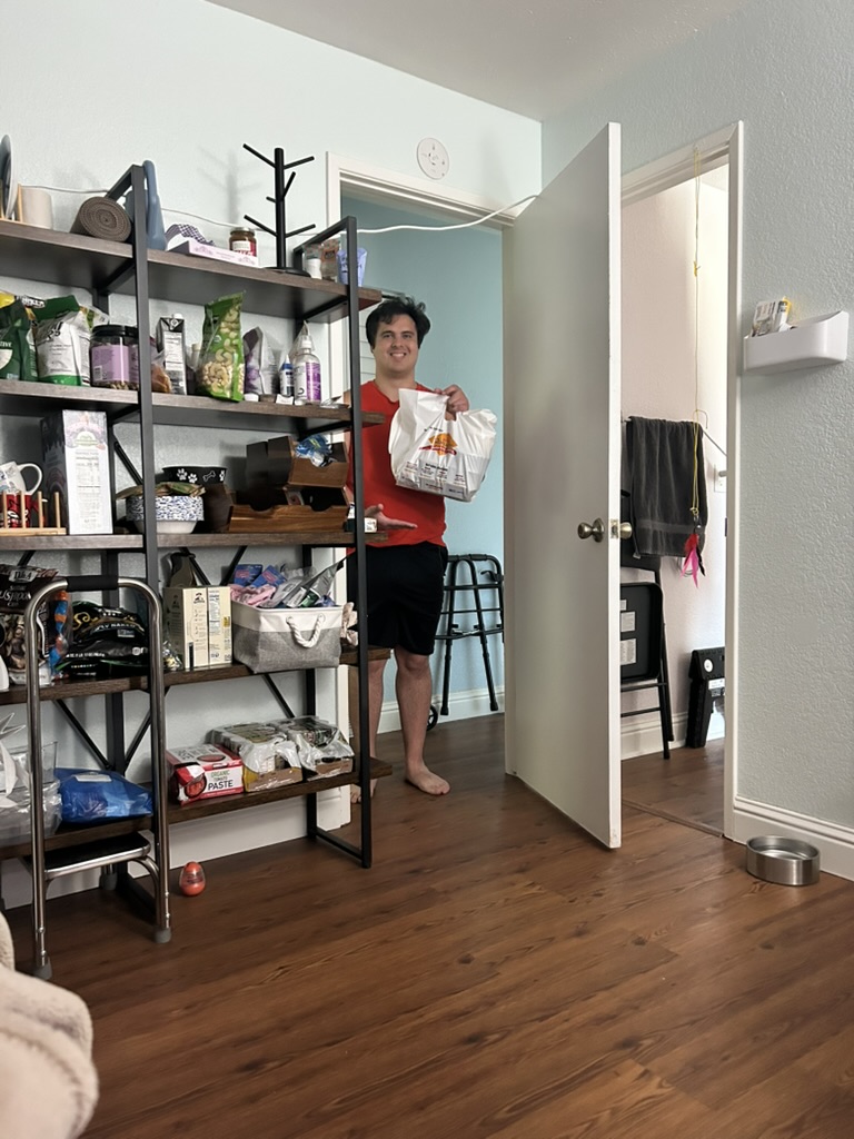 Nick standing at the doorway holding a bag of takeout food, just arriving back with a second delivery.