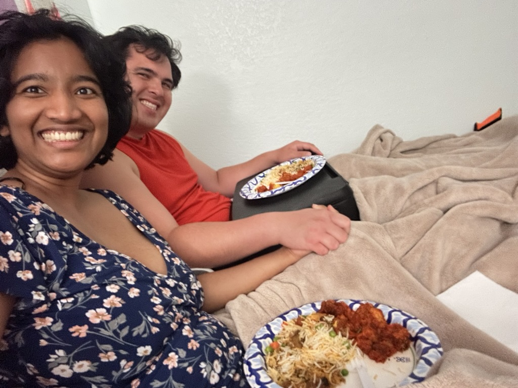Harshini and Nick sitting together indoors with takeout food placed in front of them, preparing to eat.