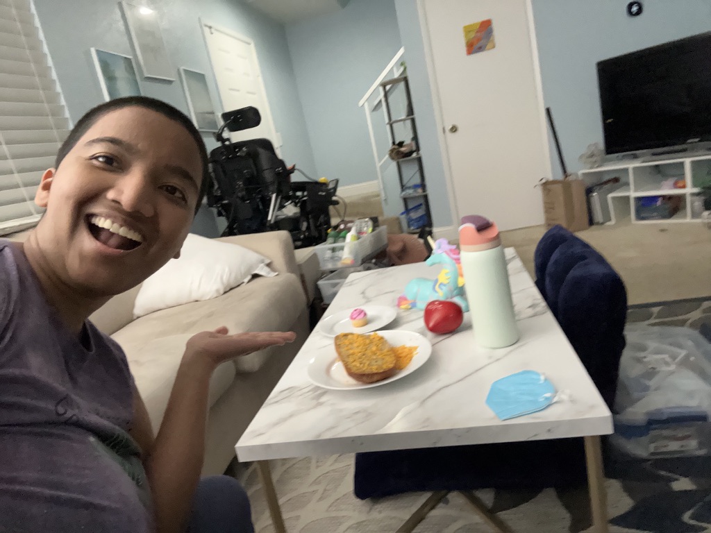 Harshini presenting a small celebration meal of garlic bread and a cupcake on a coffee table at home.
