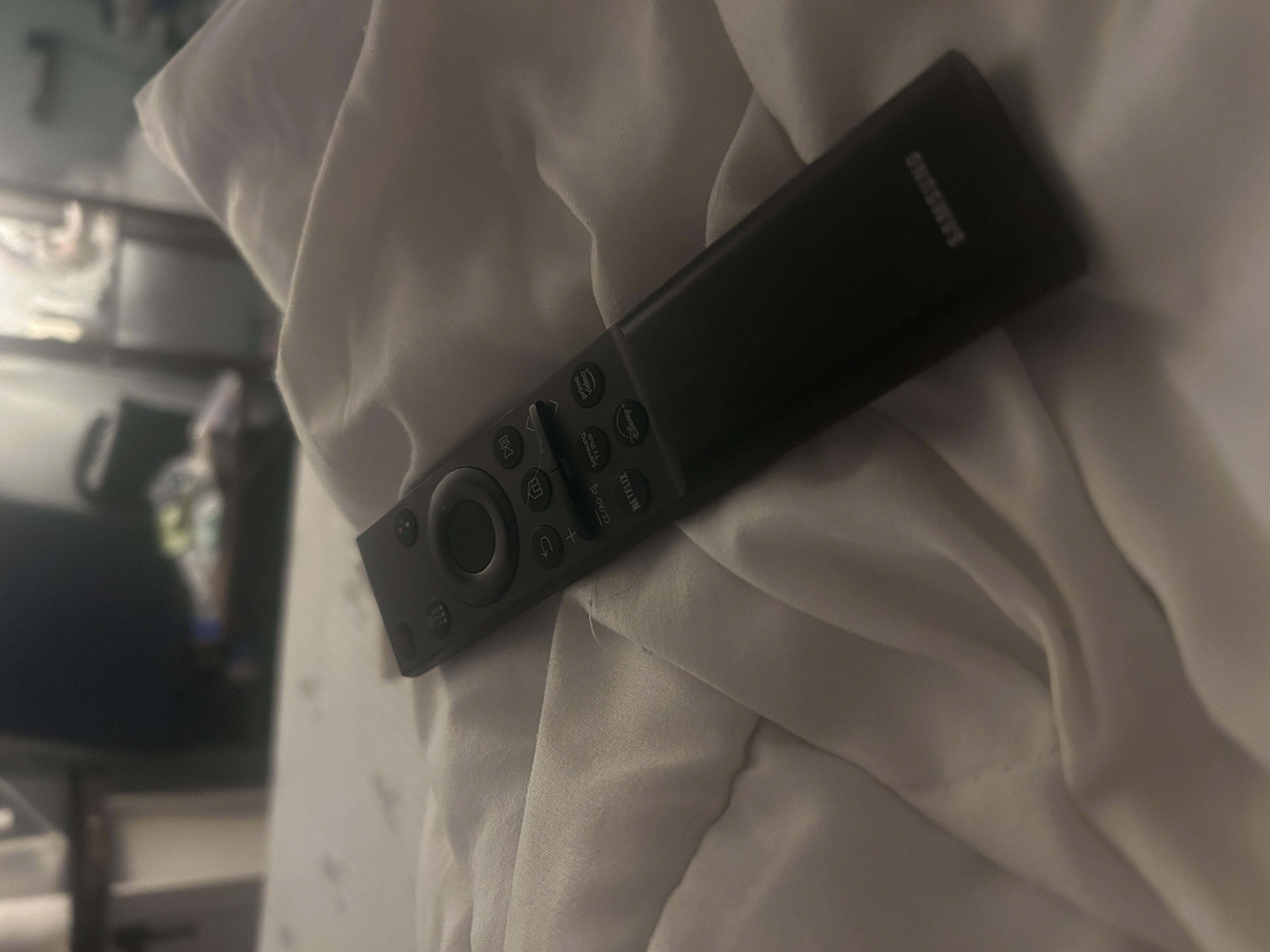 A black TV remote placed on a white blacket on the bed.