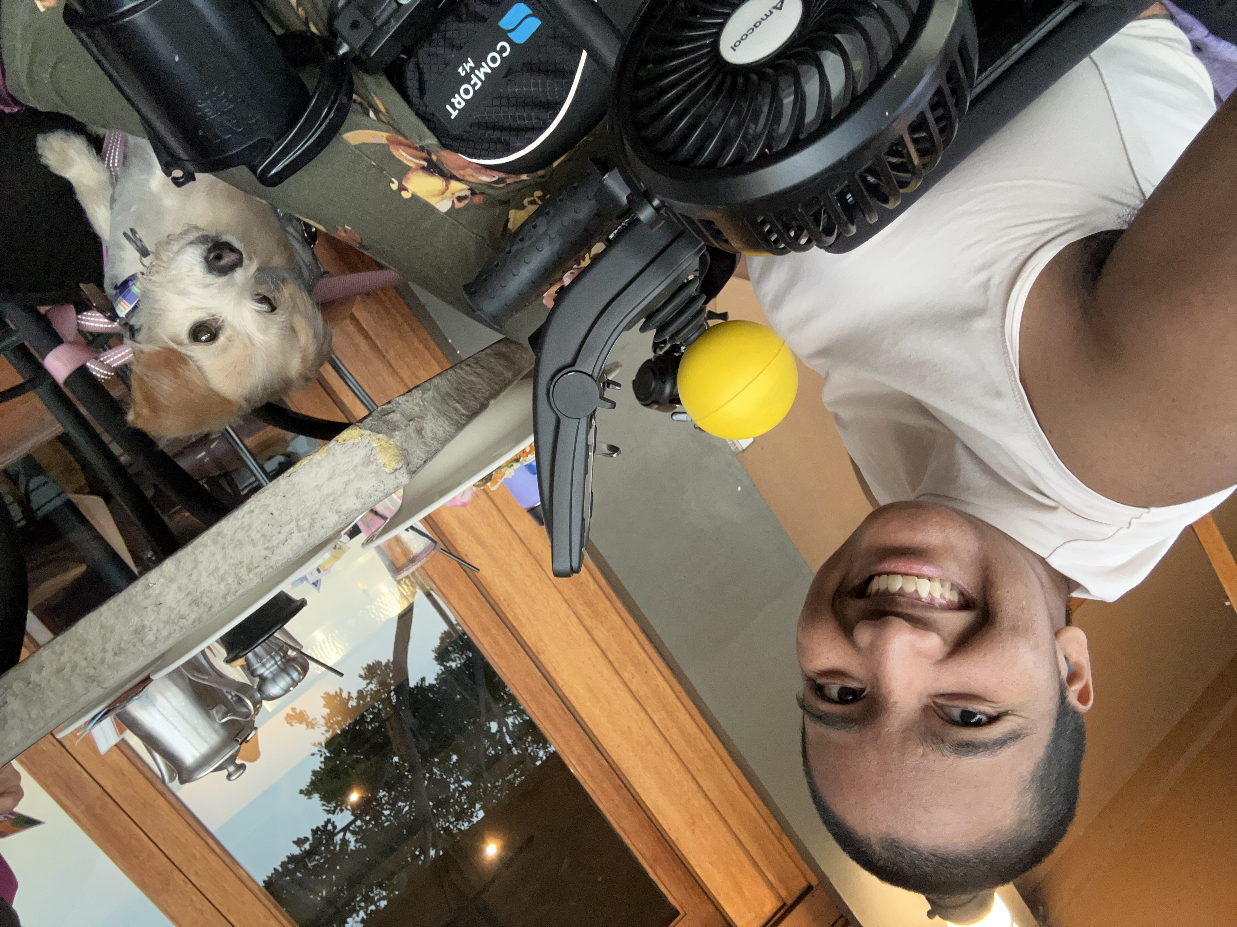 Harshini smiles beside Toffee while seated in her power wheelchair at an outdoor restaurant.