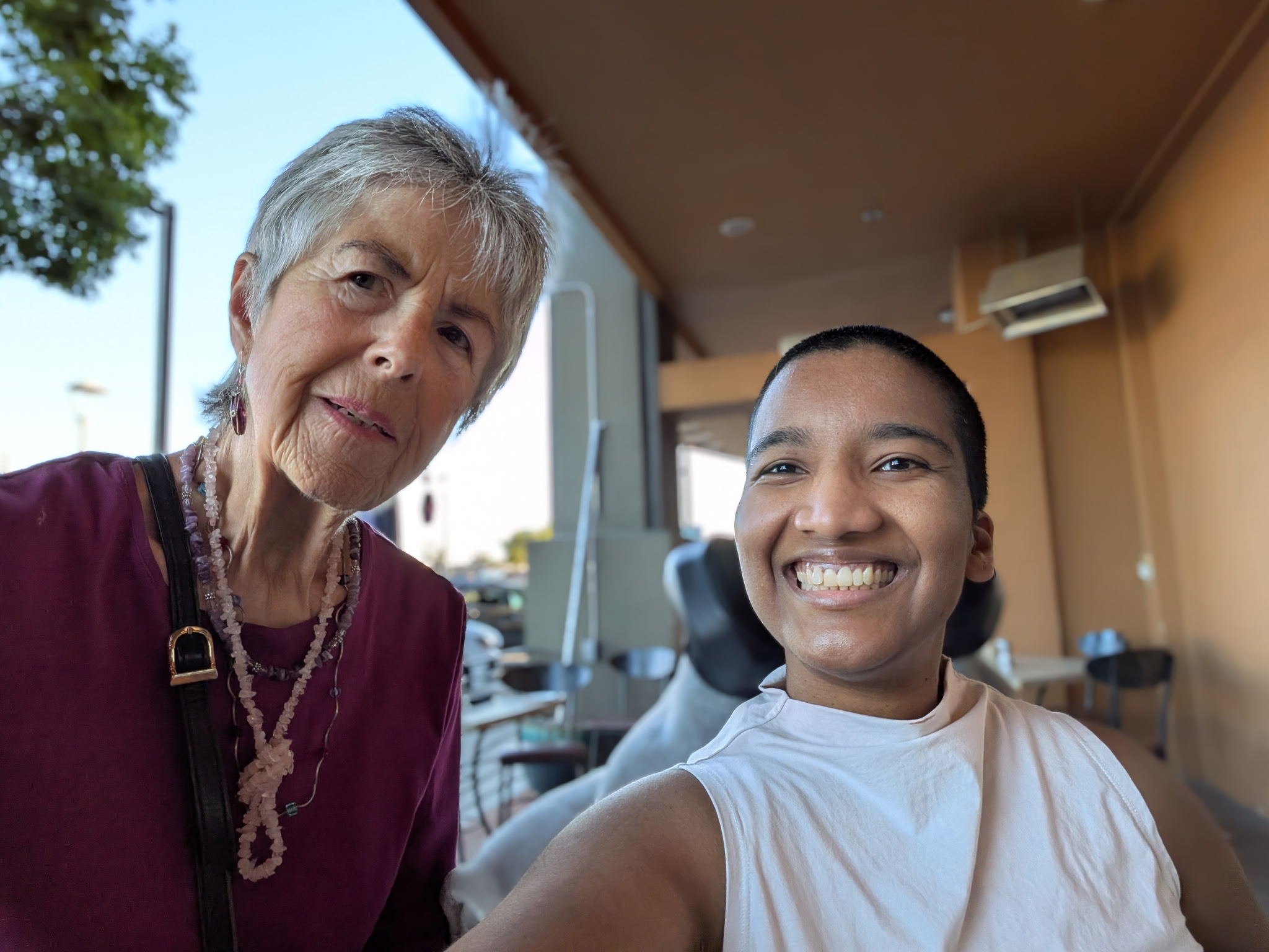Harshini and her neighbor smile together for a selfie on the restaurant patio.