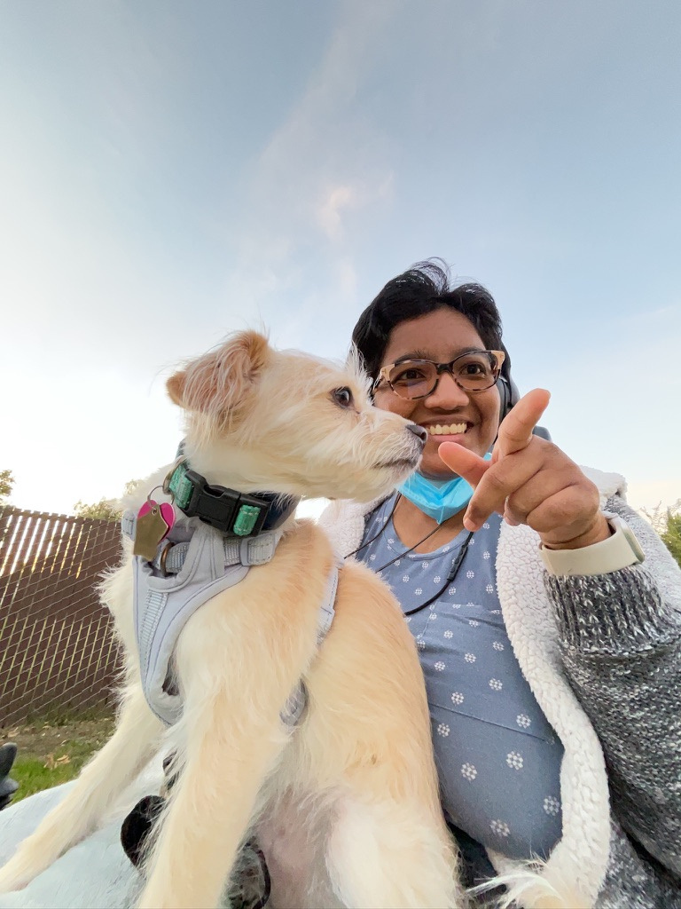 Harshini outdoors holding her dog in her lap, smiling as she gently points her dog toward the camera.